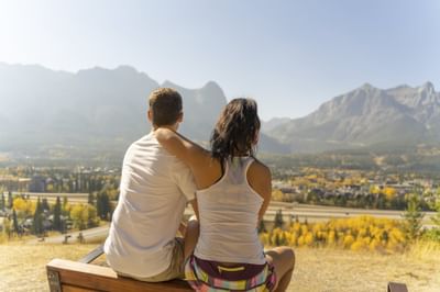 Couple sitting on a bench, embracing as they overlook a scenic valley surrounded by mountains at Blackstone Mountain Lodge