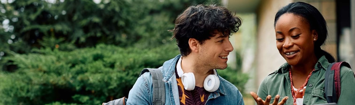 Two students with backpacks talking & one holding a laptop outdoors at UniLodge Canada