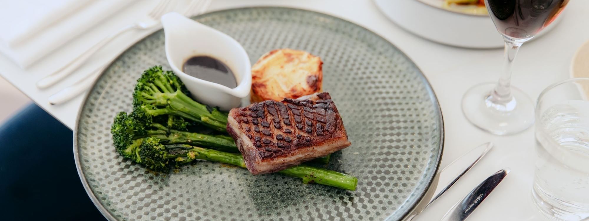 350 Lounge & Barat Novotel Sydney Parramatta, Plate with broccoli, asparagus, sauce, fork, and a wine glass on a table 