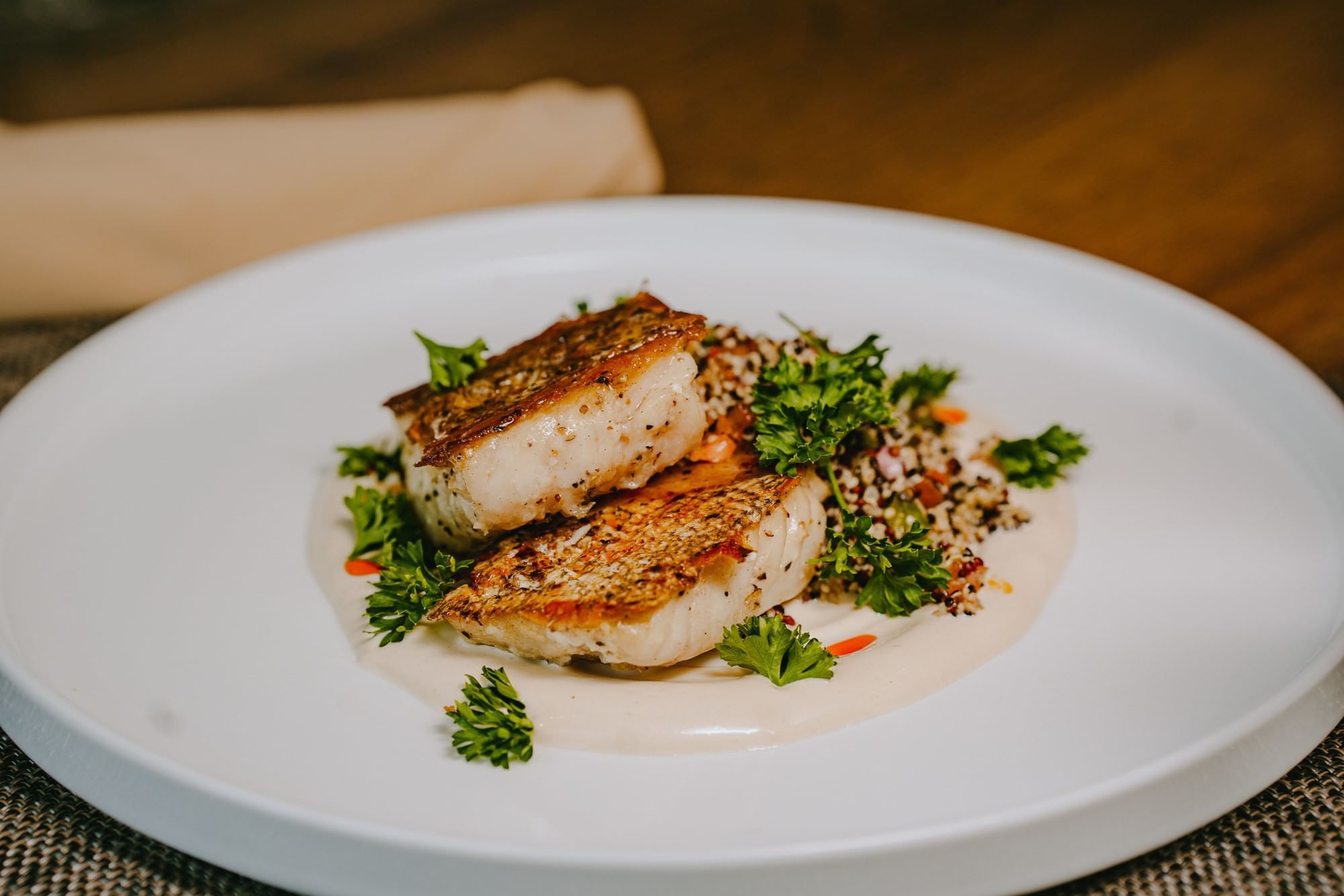 Plate with two pieces of fish, white sauce, and garnish of parsley and carrots on a wooden table.