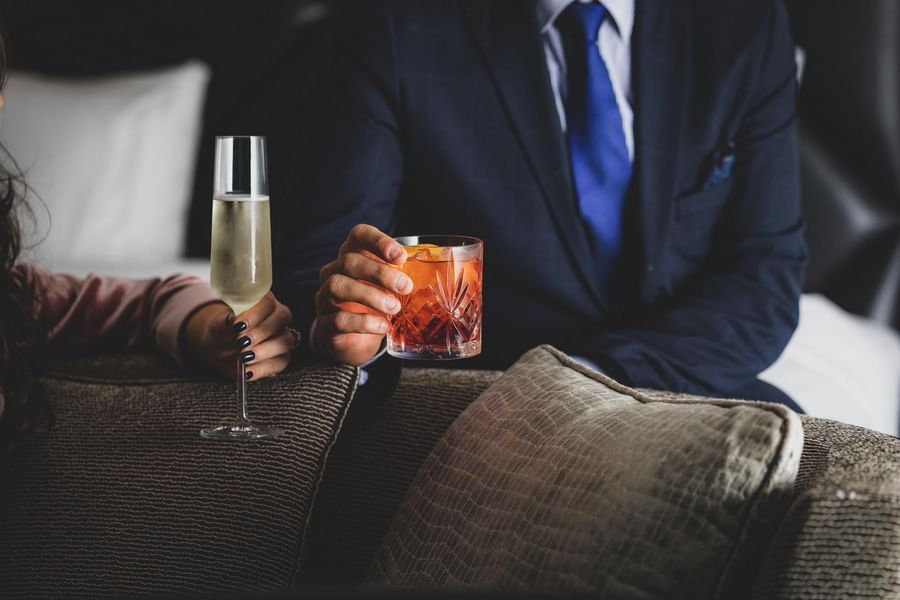 Man in a navy suit holding an old-fashioned cocktail next to a woman holding a champagne flute at The May Fair Hotel