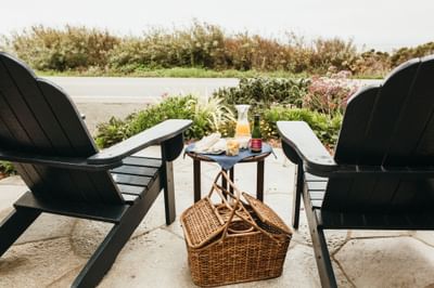 Two black chairs with a picnic basket and small table with food and drinks between them.