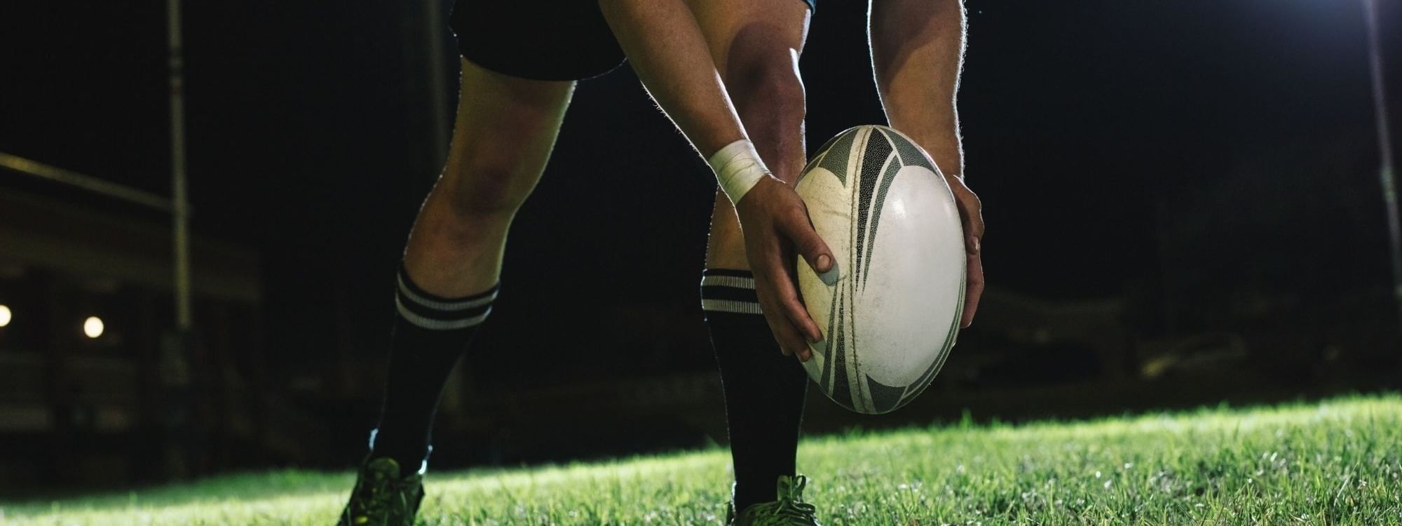 Rugby player holding ball on illuminated field at night for Bledisloe Cup Dining experience