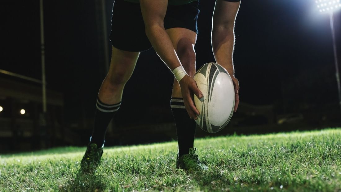 Rugby player holding ball on illuminated field at night for Bledisloe Cup Dining experience