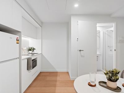 White kitchen and dining area with appliances, wooden floors, and modern furniture.