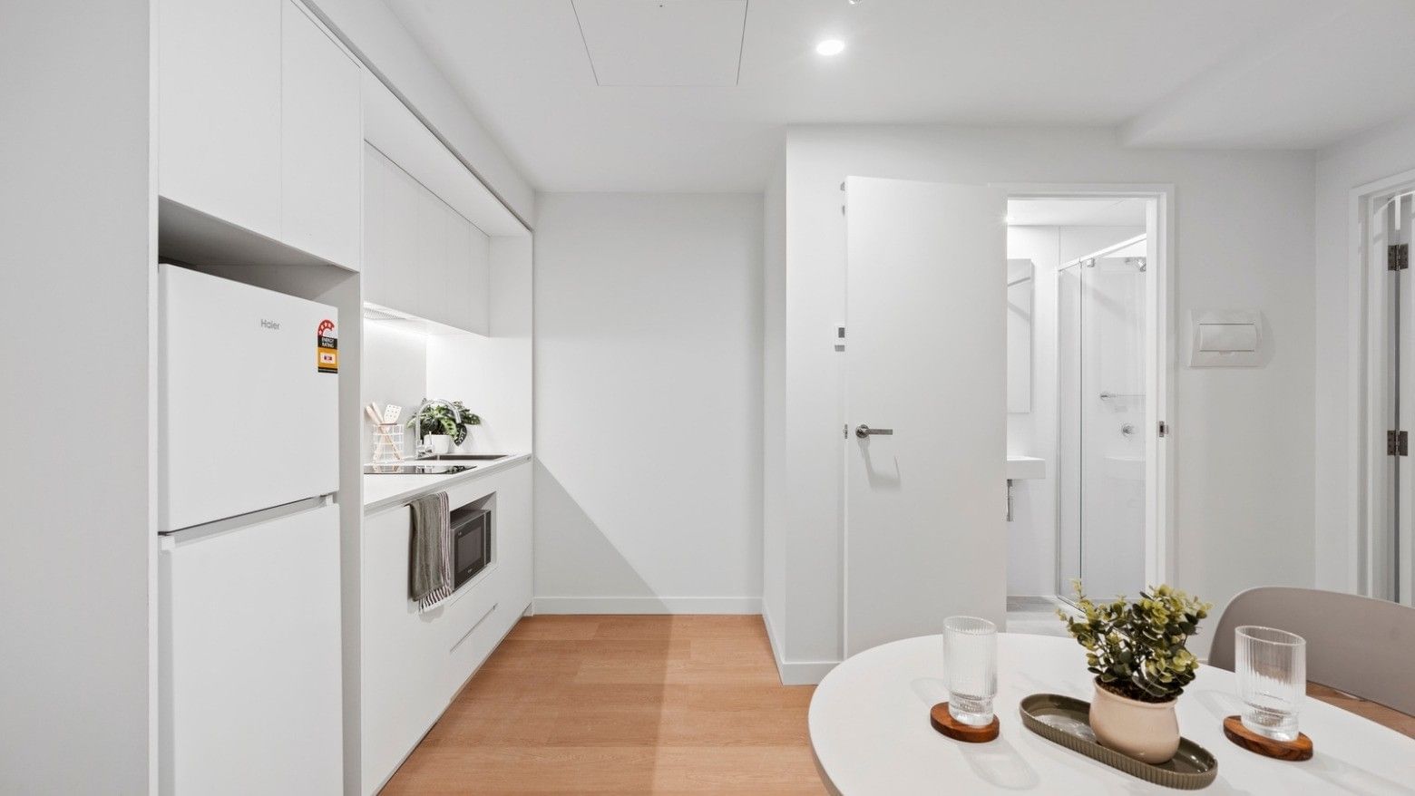 White kitchen and dining area with appliances, wooden floors, and modern furniture.