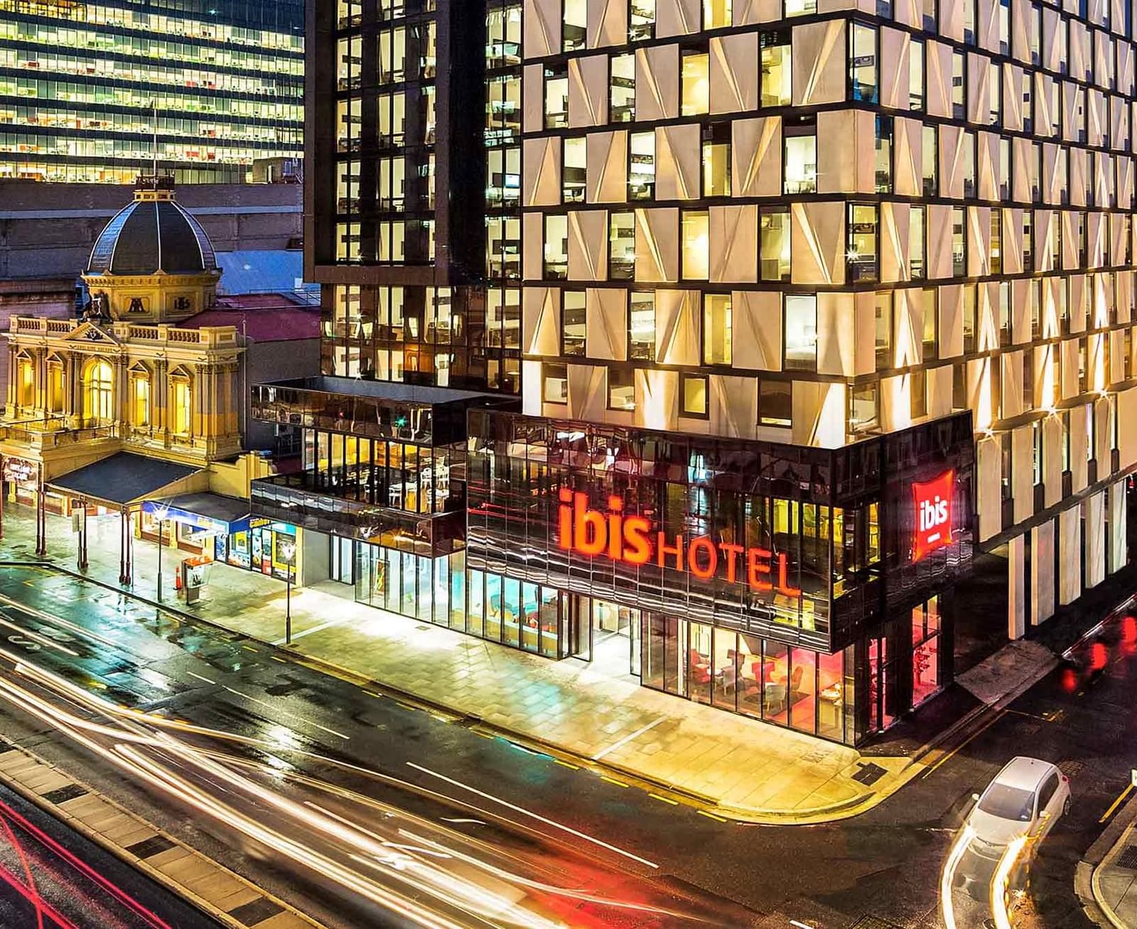 Exterior view of the Ibis Adelaide with illuminated windows, and blurred light trails from city traffic