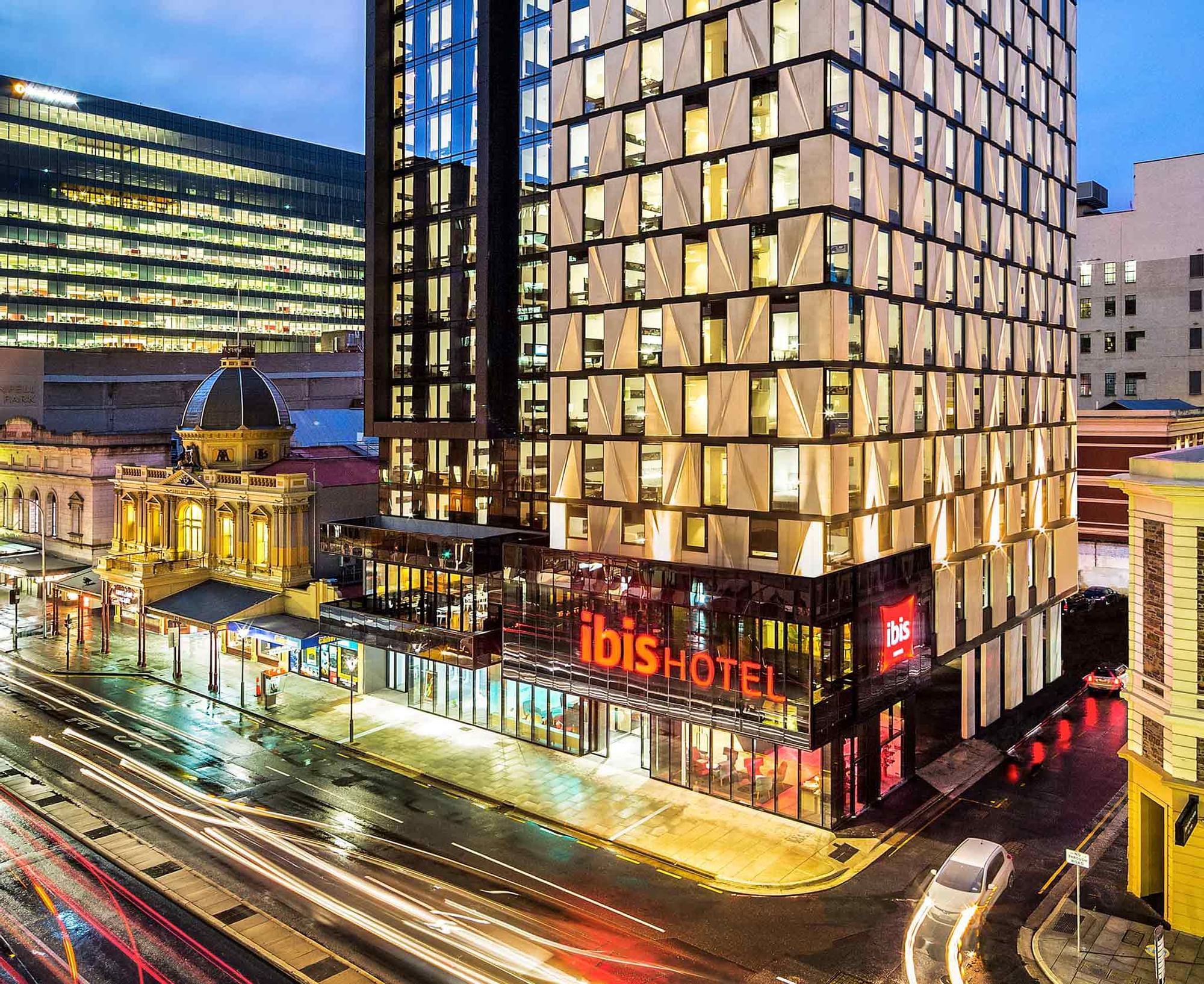 Exterior view of the Ibis Adelaide with illuminated windows, and blurred light trails from city traffic