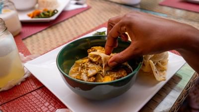 Diner's hand takes a piece of roti to dip into a bowl of curry on a white plate at Worthing Court Apartment