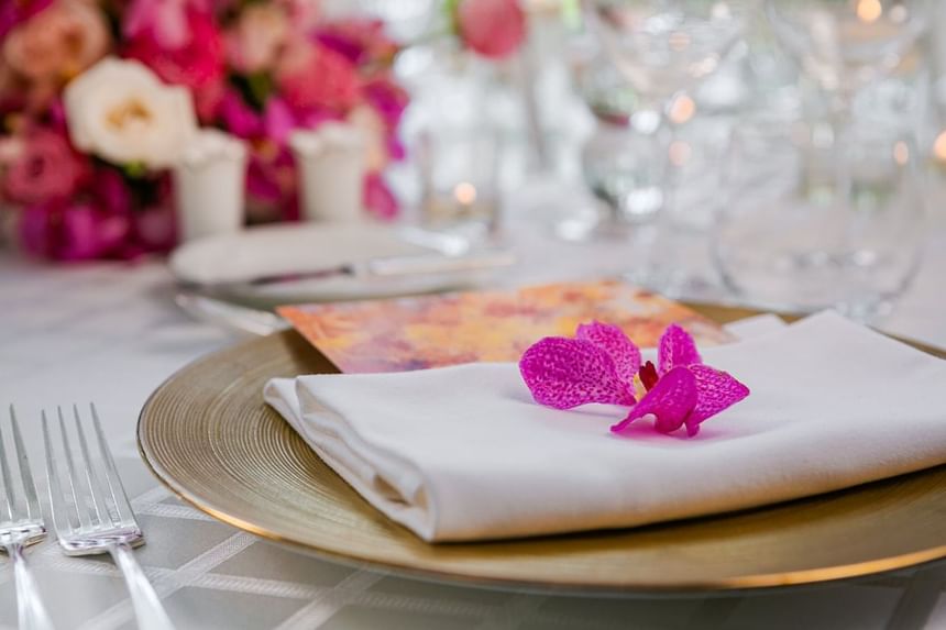 Dining table featuring a gold plate, white napkin, and vibrant purple orchid, with floral arrangements at Park Hyatt Saigon