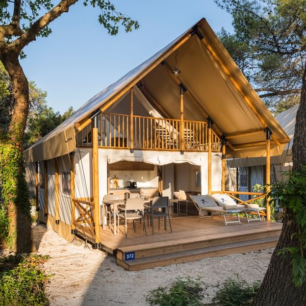 Tenda glamping con terrazza e mobili da pranzo, circondata da alberi da Falkensteiner Group