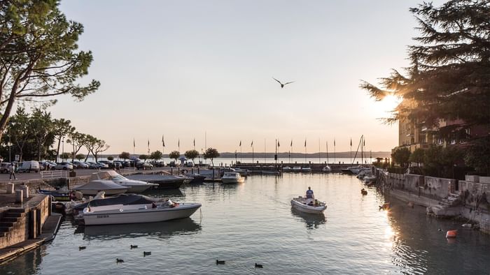 Sunset at a tranquil lake with boats and trees near Falkensteiner Park Resort Lake Garda