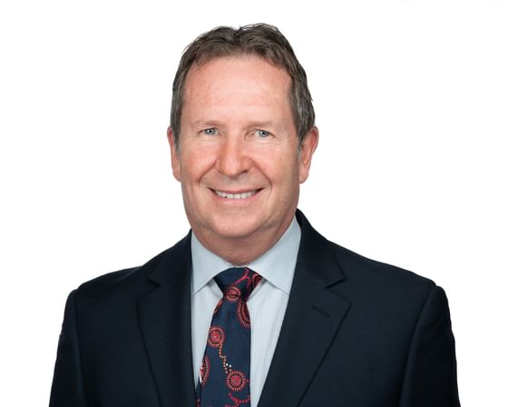 A man in a suit and tie smiles against a plain white background.