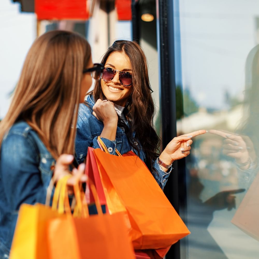 Two women shopping with orange bags outside a store at Warwick Melrose Dallas.