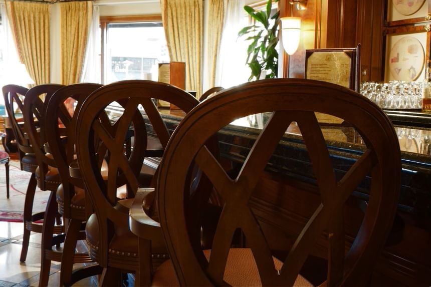 Elegant wooden bar stools with distinctive backs line a polished bar in The Rose Hotel