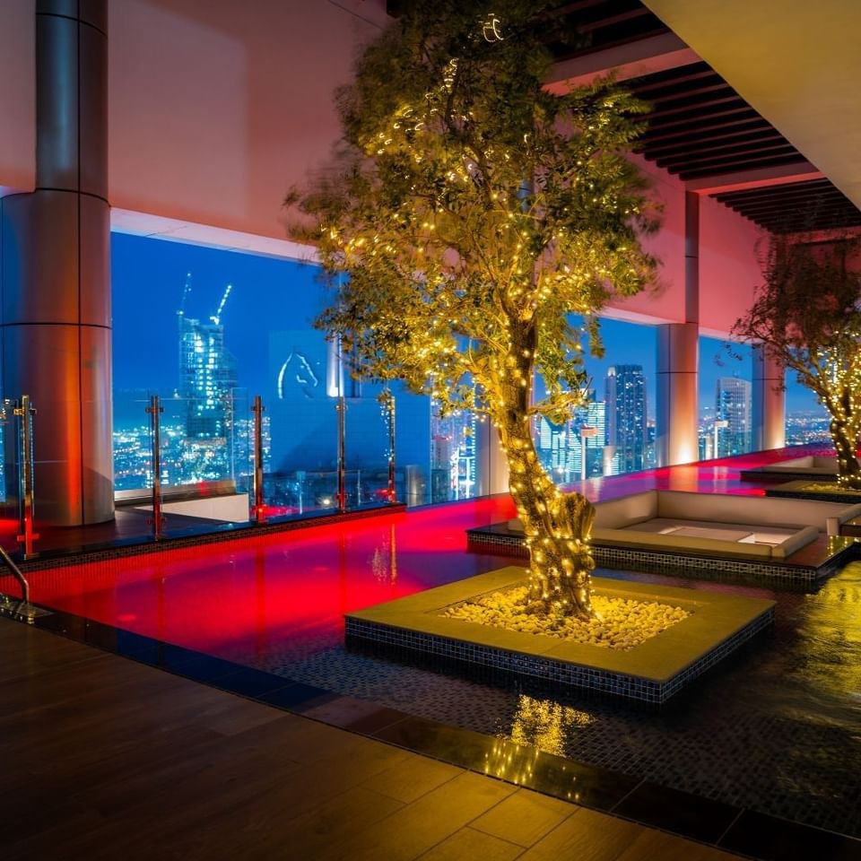 Illuminated tree with fairy lights beside an Indoor Terrace pool overlooking the night city view at Malibu Sky Lounge & Bar