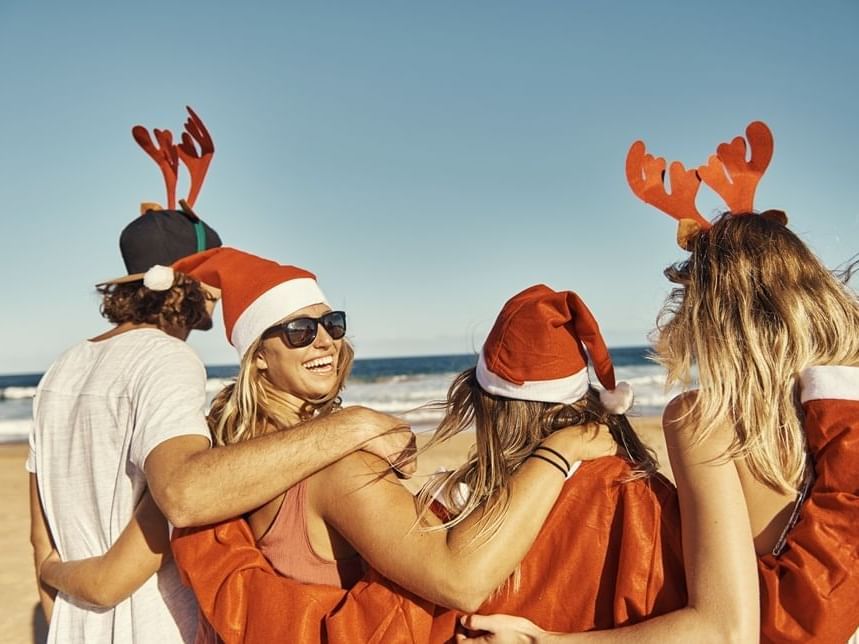 Four people laughing on the beach in Christmas clothes