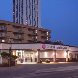 Illuminated hotel entrance with COAST hotels by APA signage at dusk at Coast Calgary University Area Hotel by APA