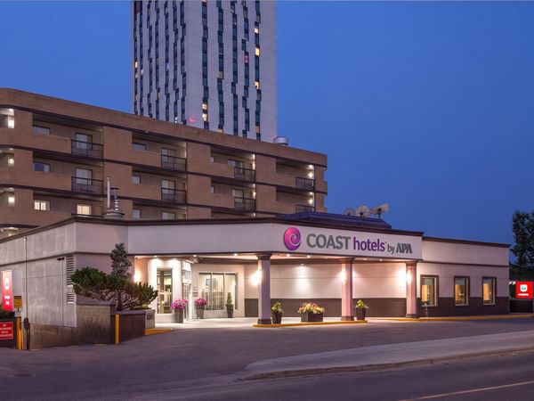 Illuminated hotel entrance with COAST hotels by APA signage at dusk at Coast Calgary University Area Hotel by APA
