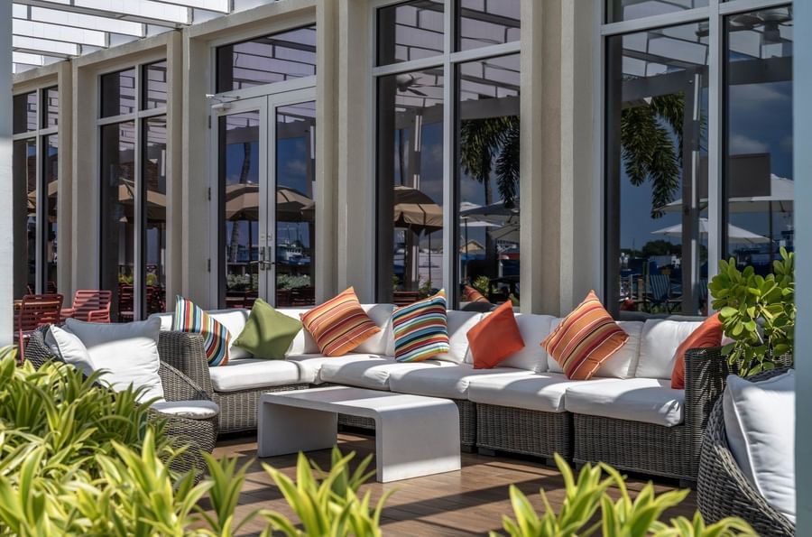 Wicker sofas by a stone table under large windows surrounding pillows in Verandah at Warwick Paradise Island Bahamas