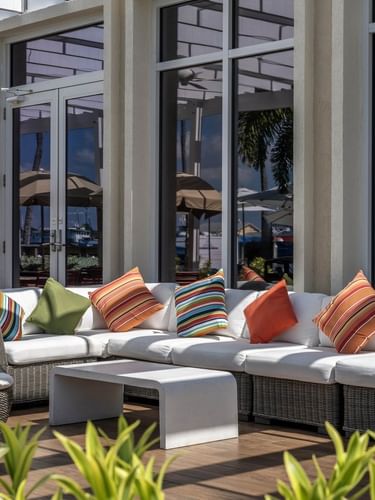 Wicker sofas by a stone table under large windows surrounding pillows in Verandah at Warwick Paradise Island Bahamas
