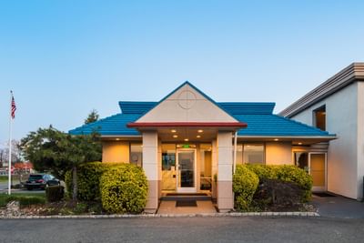 Welcoming exterior of the Garden Executive Hotel, featuring a vibrant blue roof, lush green bushes, and an American flag