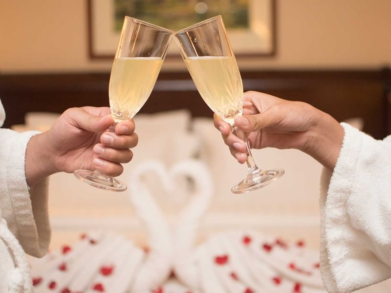 Close-up of a couple toasting champagne glasses on a bed with rose petals at Sunway Hotel Phnom Penh
