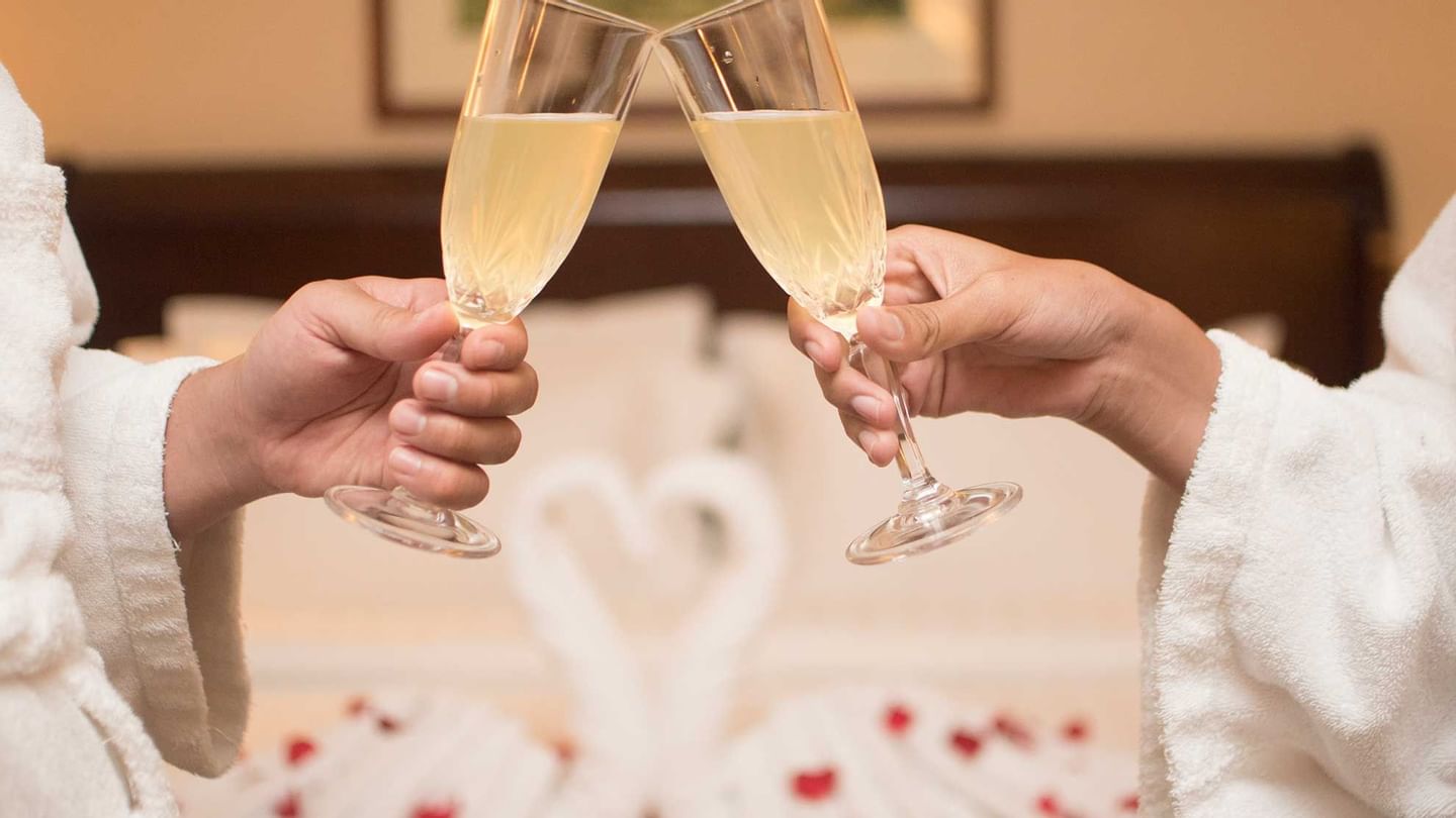 Close-up of a couple toasting champagne glasses on a bed with rose petals at Sunway Hotel Phnom Penh