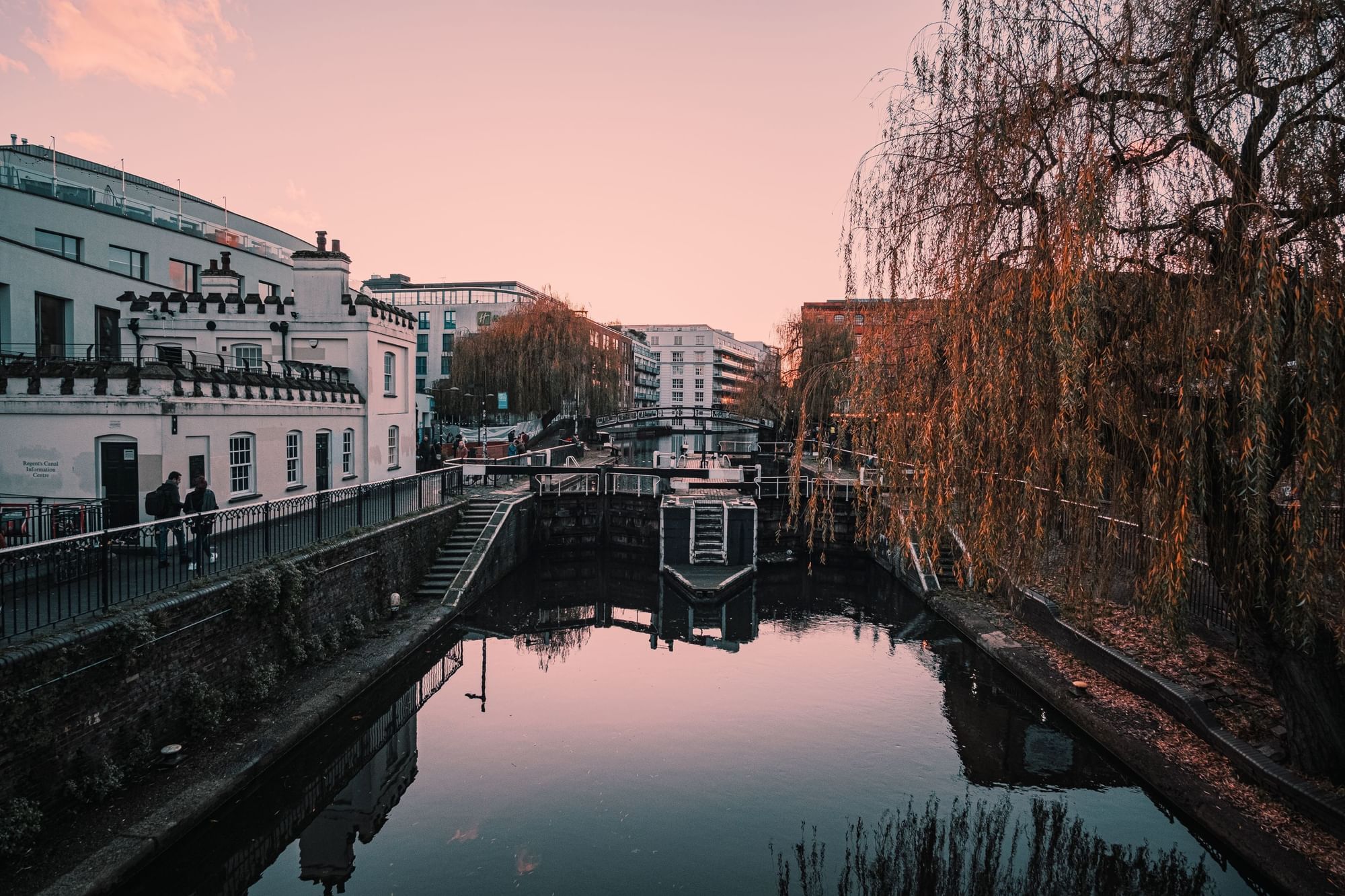 Serene sunset view of Camden Lock with water reflections, trees, and historic buildings near The Londoner