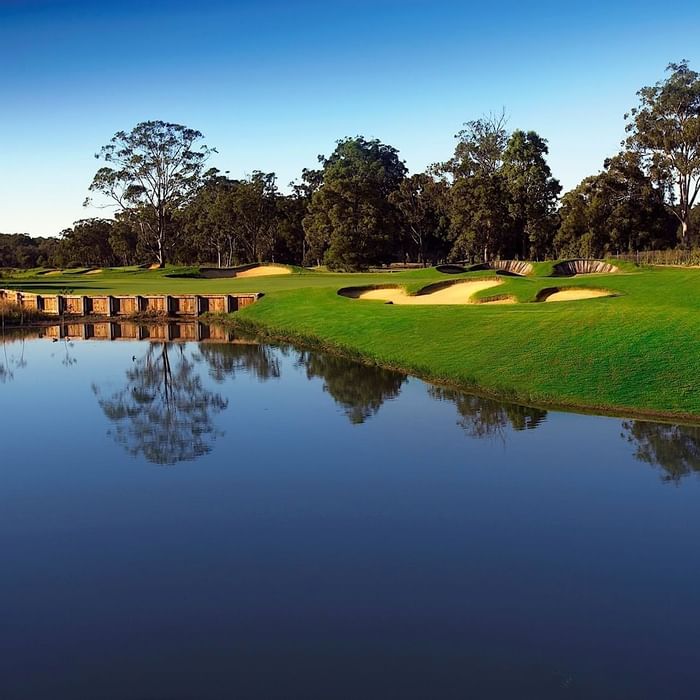 A tranquil golf course with sand bunkers reflected in a still pond near Mercure Kooindah Waters