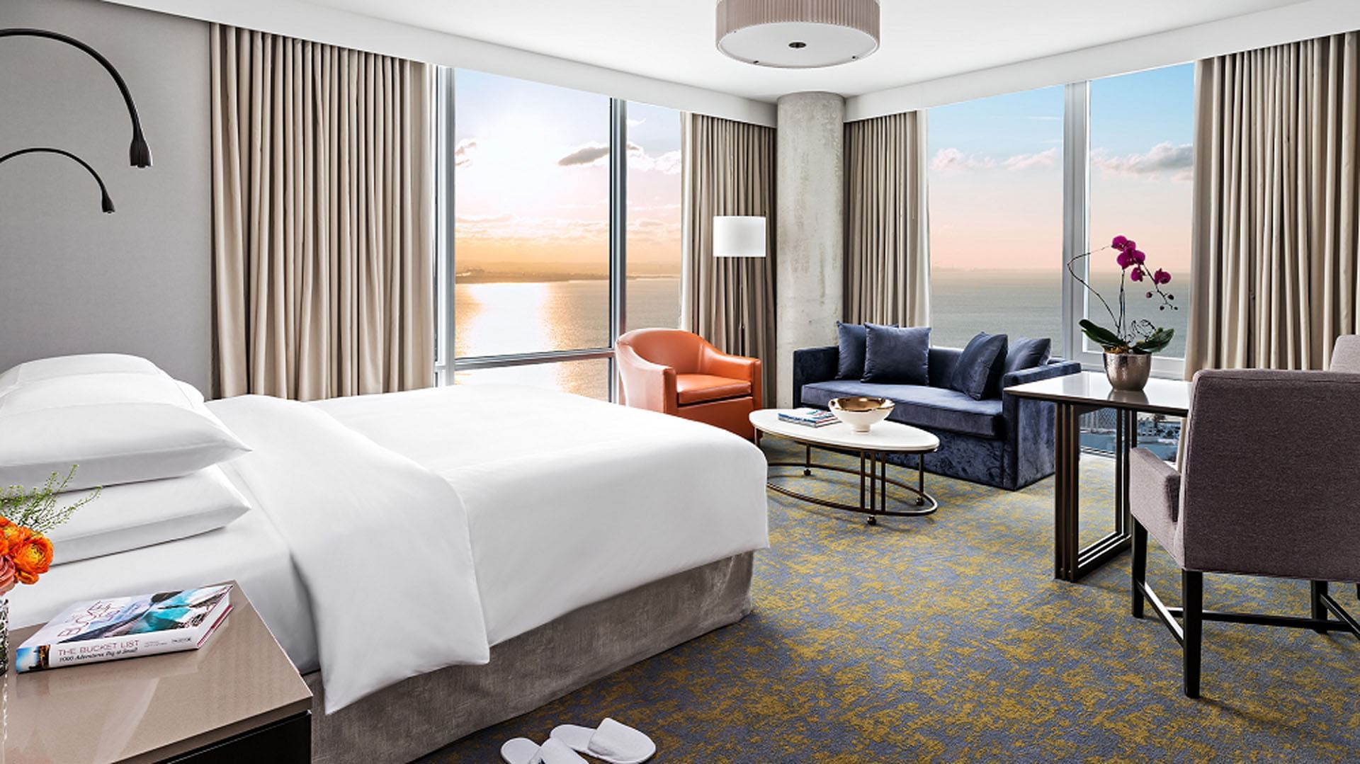 King bed facing sofa beside small seating area with floor-to-ceiling windows & lake view at Hotel X Toronto