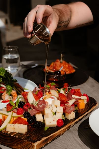 Honey drizzling over a loaded charcuterie platter with cheeses, cured meats, and fresh berries served at Gattara