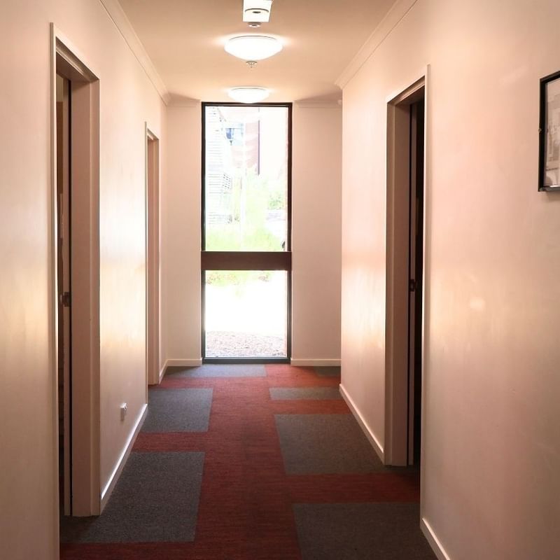 A hallway with three doors and a red floor at La Trobe University Hillside Apartments.
