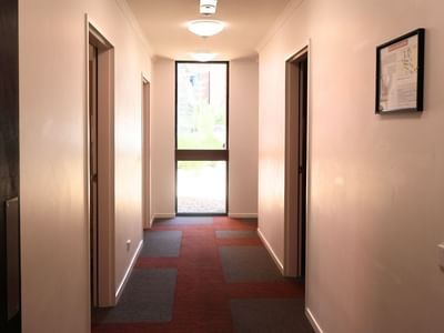 A hallway with three doors and a red floor at La Trobe University Hillside Apartments.
