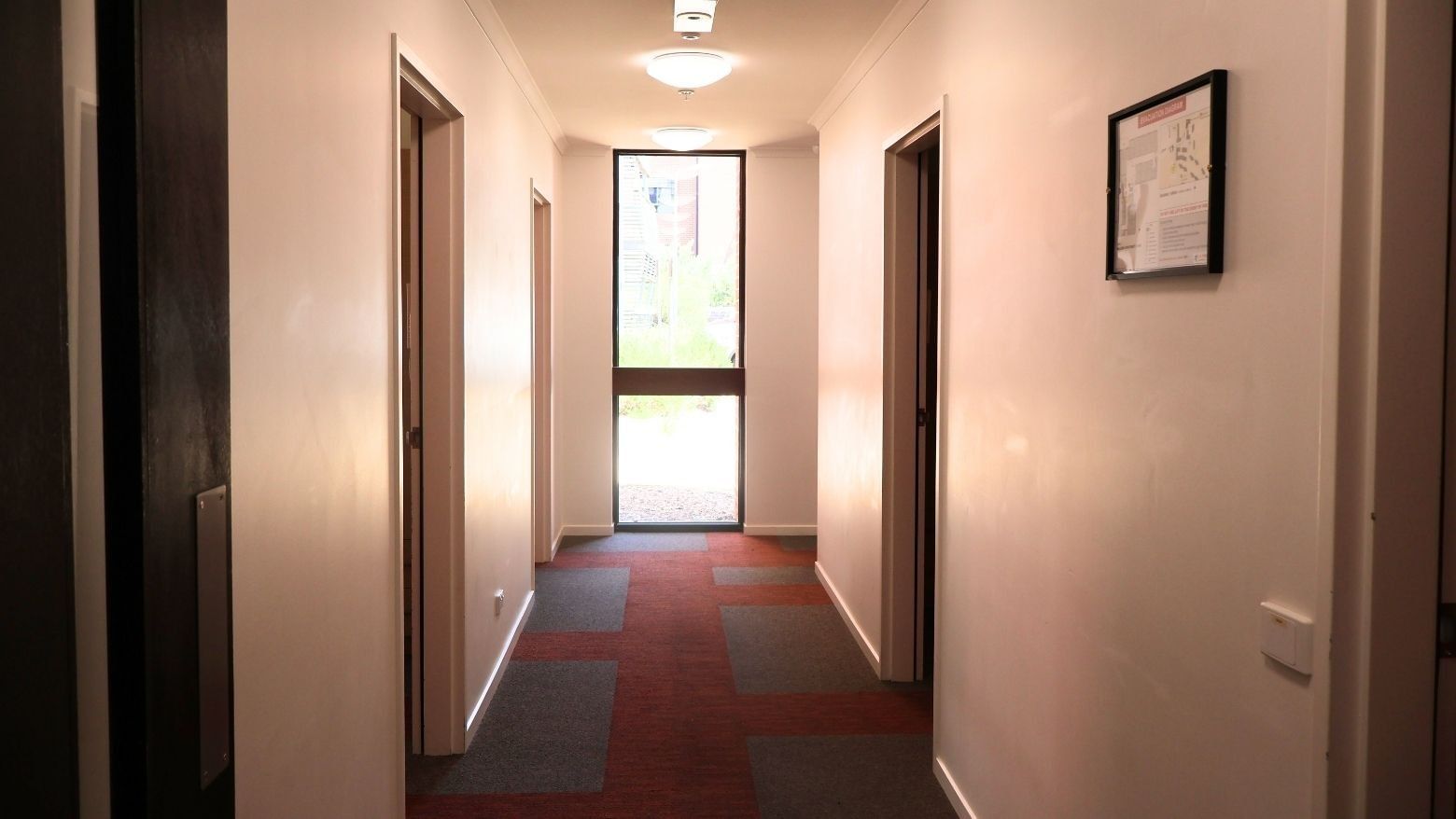 A hallway with three doors and a red floor at La Trobe University Hillside Apartments.