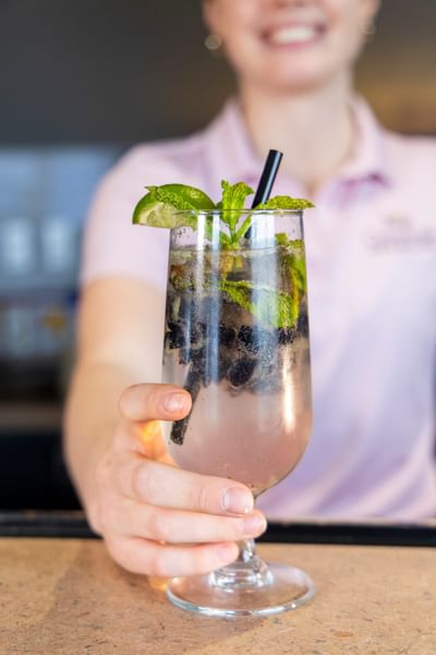 Bartender holding up a fresh blueberry mojito cocktail with mint leaves at Rodd Crowbush Golf & Beach Resort