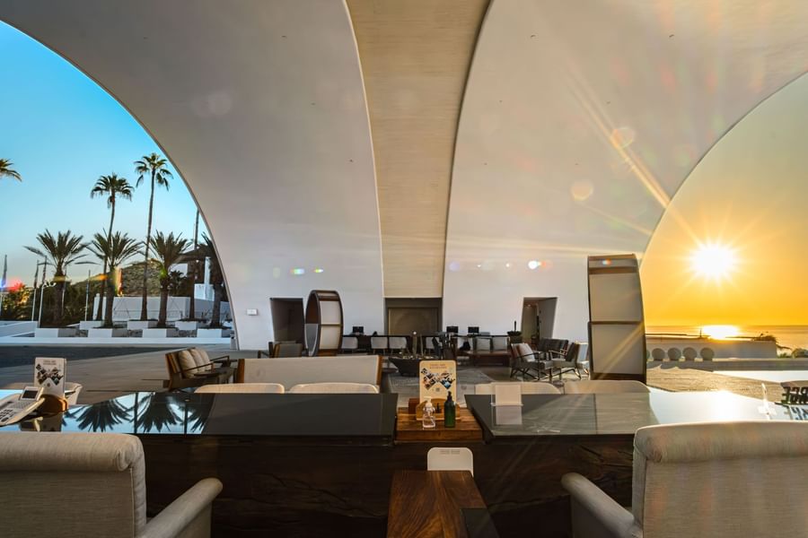 Grand lobby with curved ceiling, warm lighting, and sunset ocean views at Marquis Los Cabos Resort