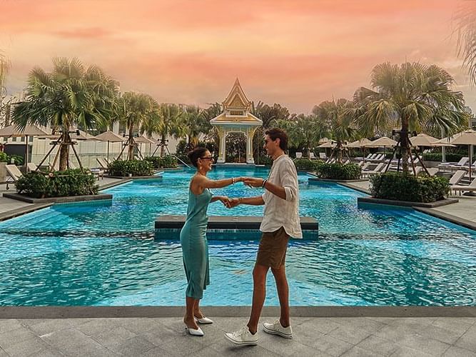 A couple stands by a pool, enjoying the serene atmosphere and beautiful surroundings.