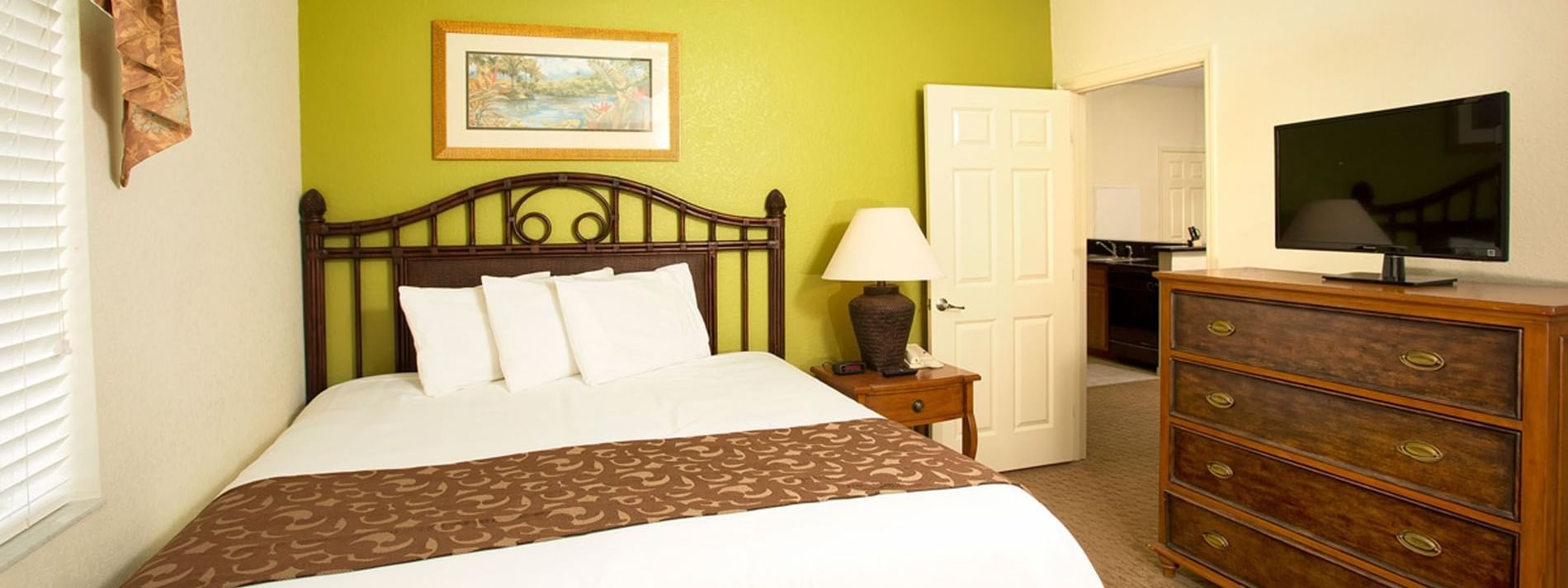 A hotel room with a bed, dresser, TV, and lamp
