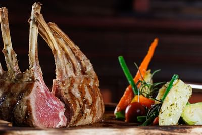 Costilla de cordero a la parrilla con coloridas verduras asadas sobre una tabla de madera en el Sunset Plaza Beach Resort, uno de los mejores hoteles con vistas a la playa en Puerto Vallarta