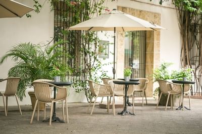 Outdoor café setup with beige chairs, small tables & blooming plants under at Billini Hotel Historic Luxury
