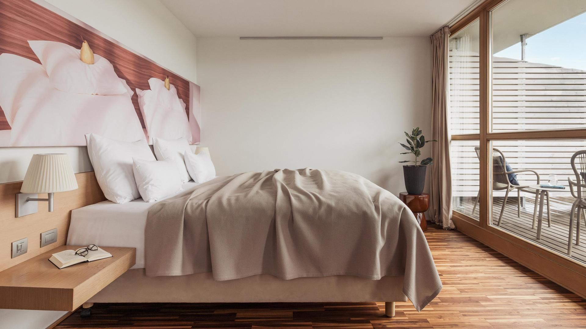 Gemütliches Hotelzimmer mit großem Bett, Holzboden und Balkon mit Aussicht.