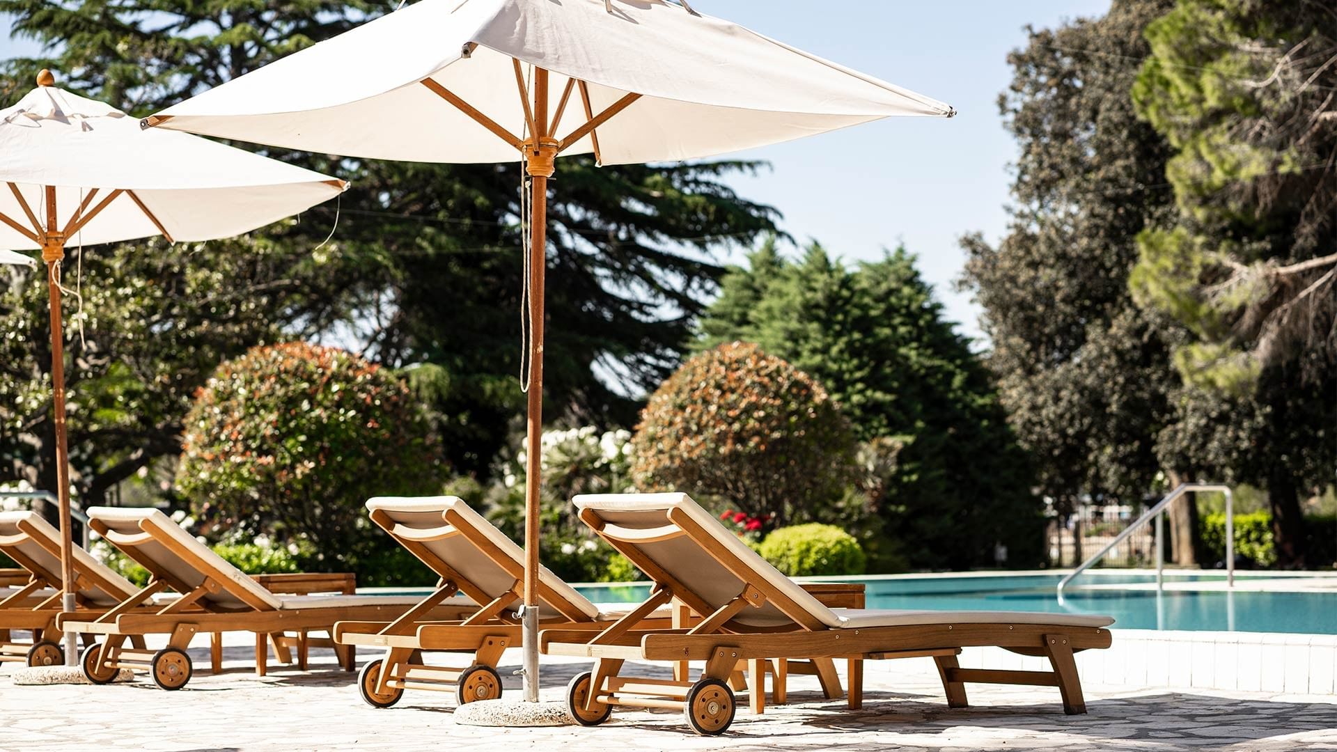 Suncobrani i ležaljke uz bazen u okruženju zelenila at Falkensteiner Group