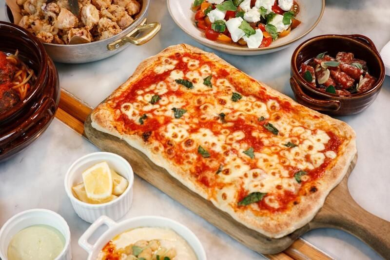 Rectangular cheese pizza on a wooden board, surrounded by various dishes at the family dinner in Park Hyatt Saigon