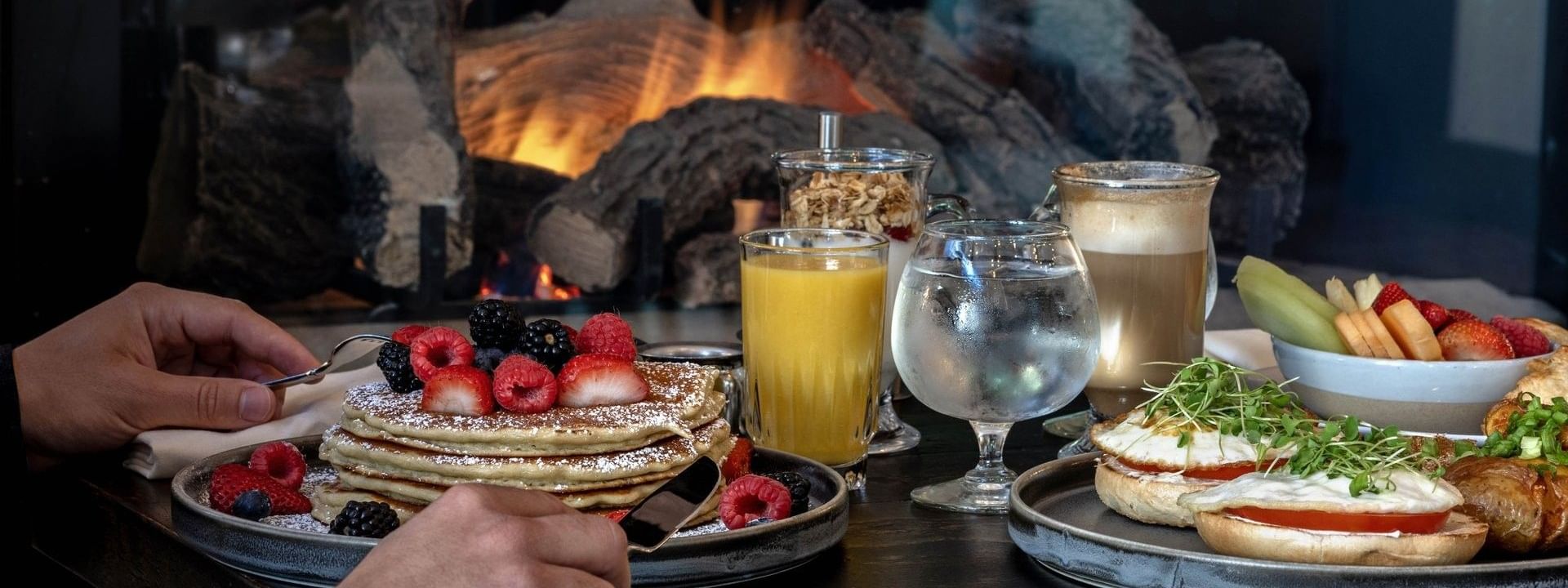Stack of pancakes with berries by orange juice under the glow of a fireplace in In-Room Dining at Warwick Denver