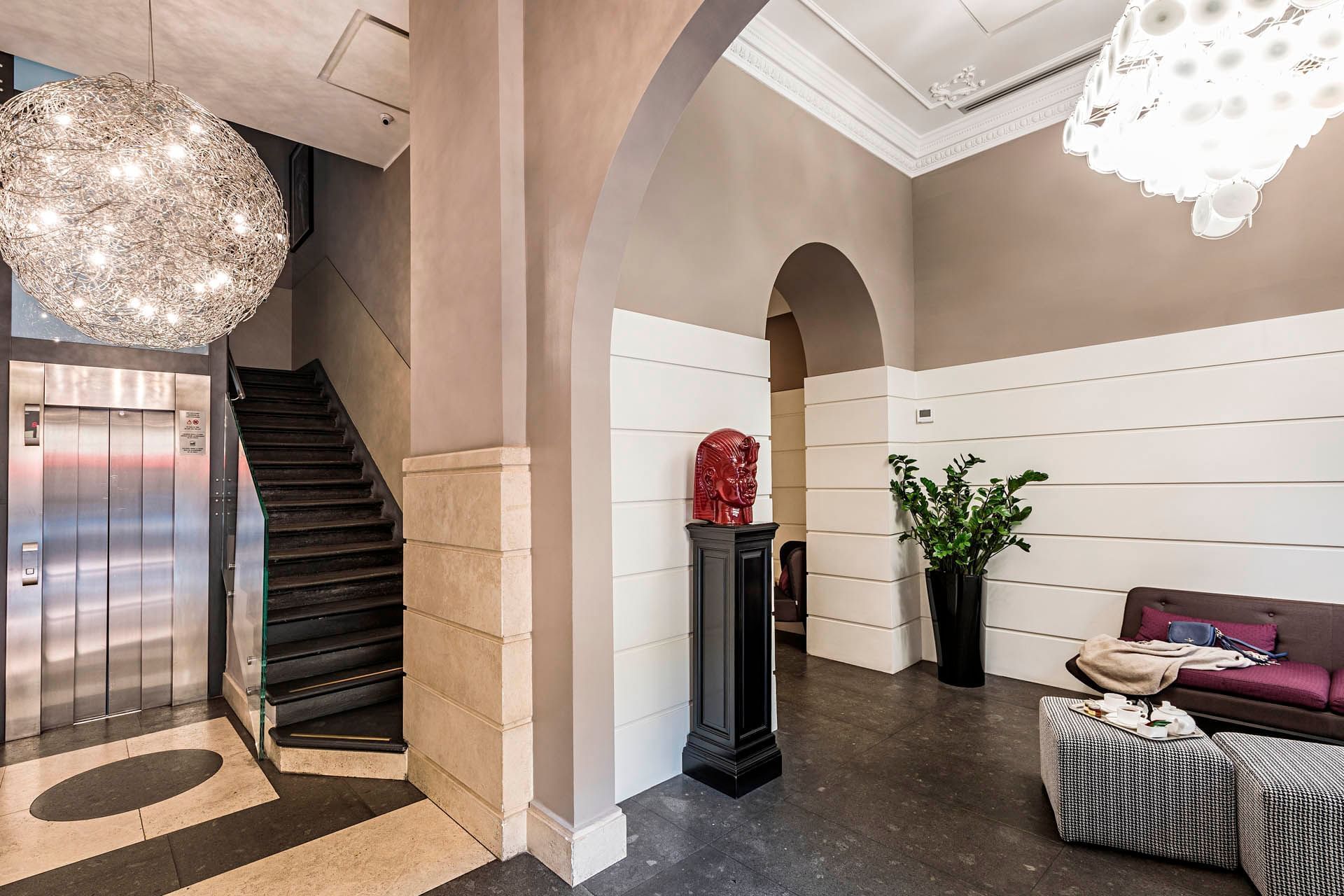 Elegant lobby at The Independent with a stylish chandelier, grand staircase, potted plant, and contemporary furniture