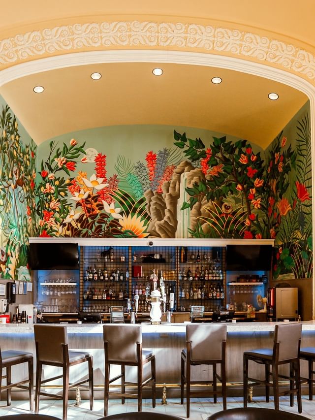 The Lobby Bar with grey stools by a colorful tropical mural under bright lights at Arlington Resort Hotel & Spa