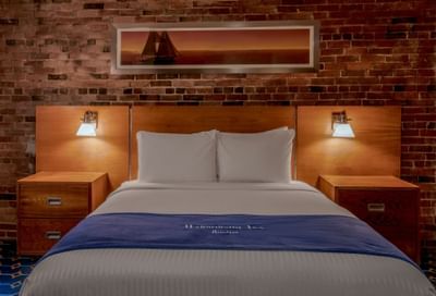Bed between the sidetables and sailboat art above the exposed brick wall in Queen Atrium View at Harborside Inn Boston
