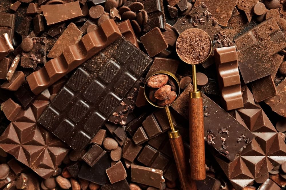 Assorted dark chocolate bars and cocoa beans by wooden spoons at Warwick Geneva