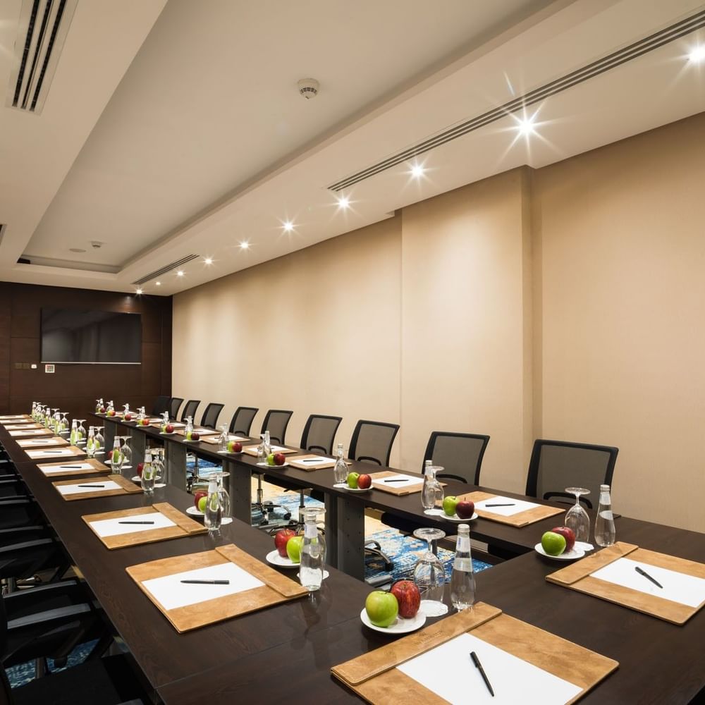 U-shaped table setup facing hanging TV in Khalej Meeting Room at Naviti by Warwick Dammam